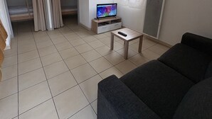 Una sala de estar con un sofá, un televisor sobre un mueble bajo, una mesita y un ventanal corredero que da a un balcón.