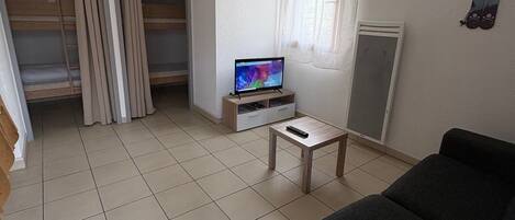 Una sala de estar con un sofá, un televisor sobre un mueble bajo, una mesita y un ventanal corredero que da a un balcón.
