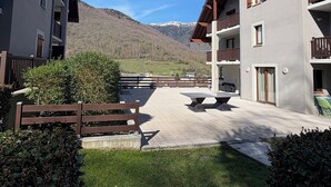Un edificio moderno con balcones, un patio empedrado y montañas al fondo.