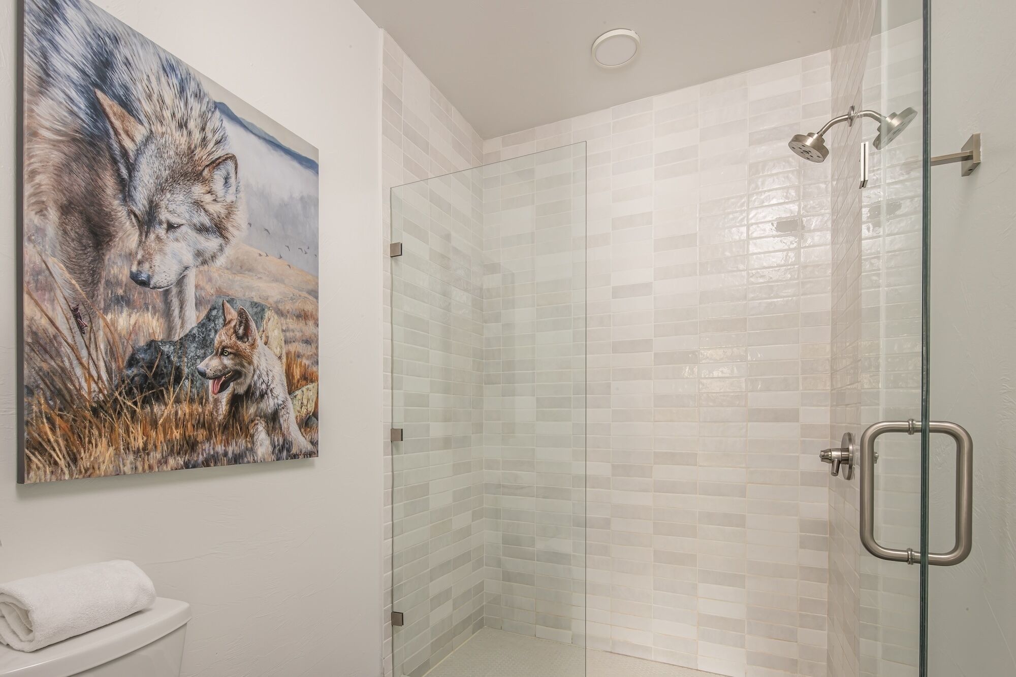 Un bagno con cabina doccia in vetro, un WC bianco e un quadro con lupi sulla parete.