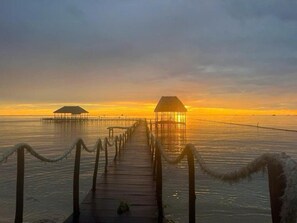 A wooden pier leading to overwater bungalows with thatched roofs, surrounded by calm water and a sunset sky. - Emerald Lagoon Retreat Phu Quoc (Phu Quoc)