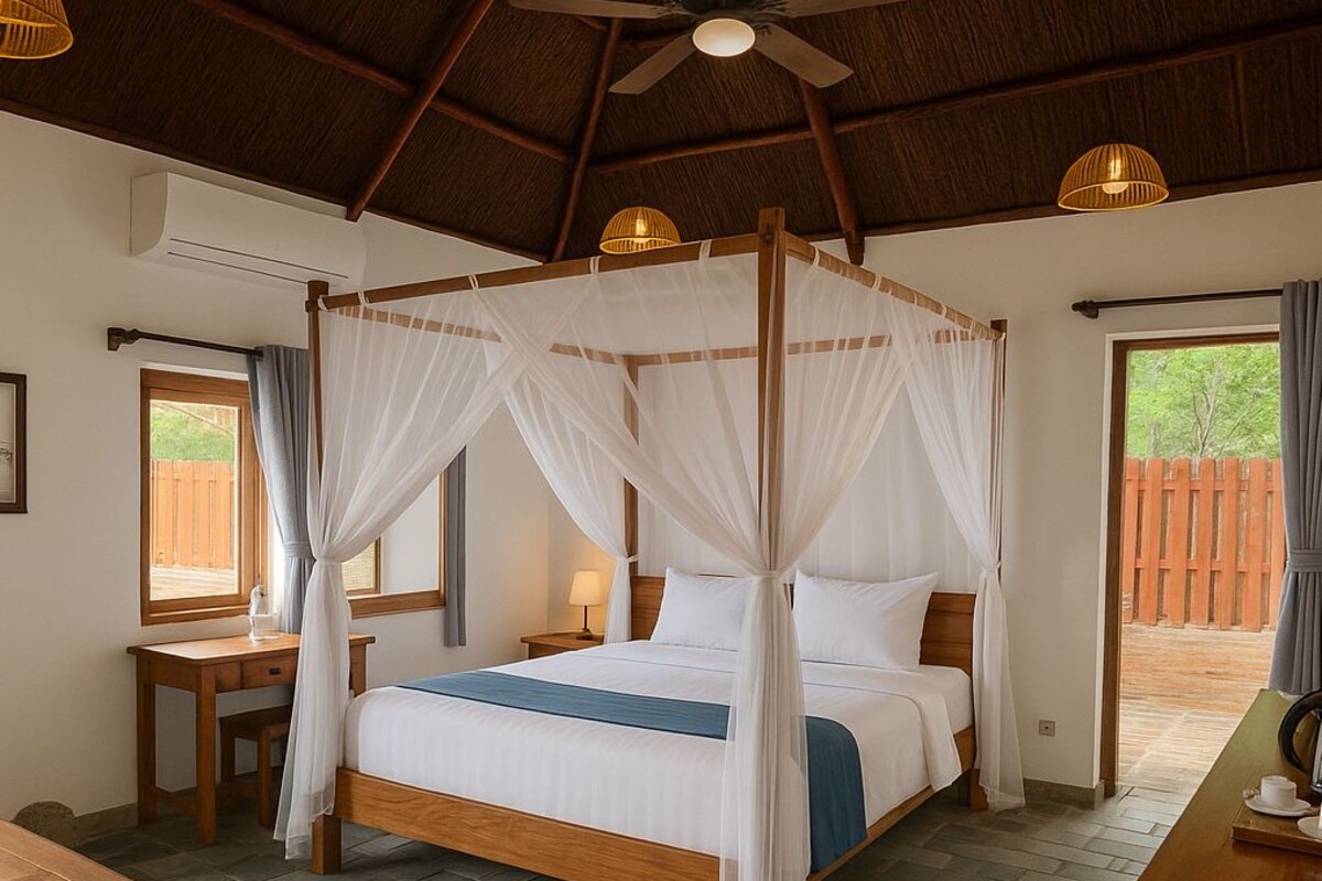 A four-poster bed with a canopy, a wooden desk, a small table, and a view of the outside.