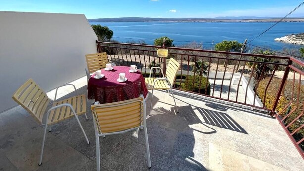 A balcony with a table and chairs, overlooking a body of water and distant land. - Apartment Luky 6 (Dramalj)