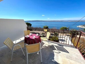 Un balcon avec une table et des chaises, donnant sur une étendue d’eau et sur une terre lointaine.