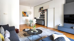 Ett modernt vardagsrum med en grå soffa, ett soffbord och en matplats med ett bord och stolar i glas.