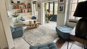 A modern living room with a sofa, armchair, and a coffee table. There is a bookshelf with books and decorative items. - L'ATTRAPE-COEURS : Charming house 6/7 persons (LA BAULE)
