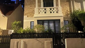 A two-story building with a stone facade, a balcony with lattice railings, and a garage with closed doors. - L'ATTRAPE-COEURS : Charming house 6/7 persons (LA BAULE)