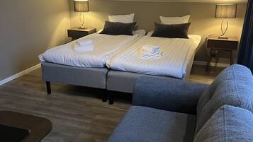 A modern hotel room with two beds, a sofa, and a small table.