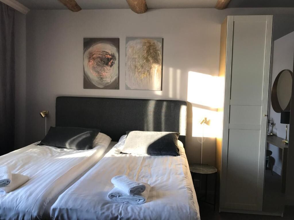 A hotel room with a large bed, two pillows, a bedside table with a lamp, and artwork on the wall.