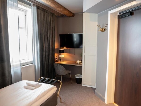 A hotel room with a bed, a desk with a TV, a chair, and a door. - Hotell gamlastaden (Kalix)