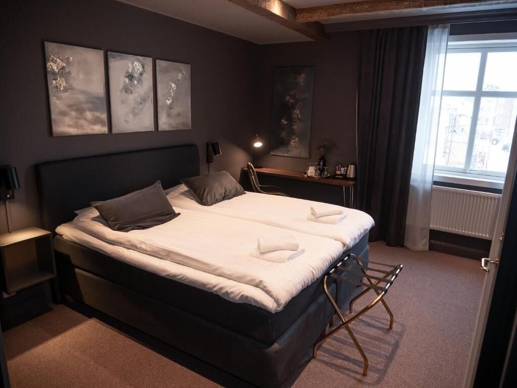 A double bed with white linens, a bedside table with a lamp, and abstract wall art.