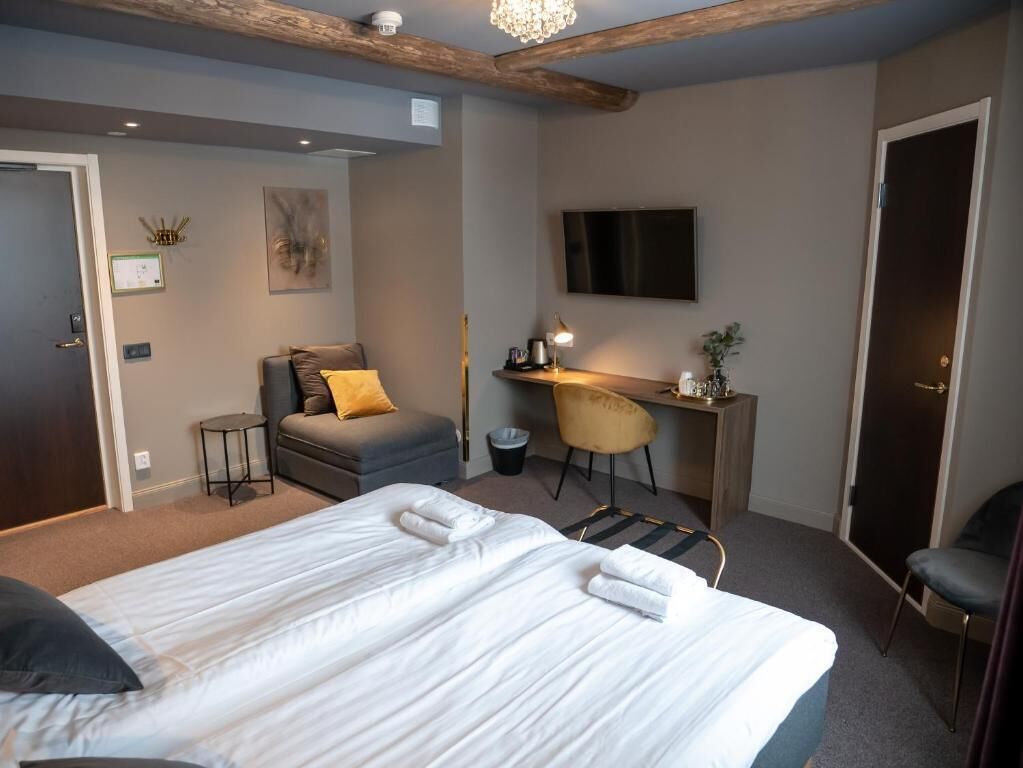 A hotel room with a bed, a desk, a chair, a TV, and a door.