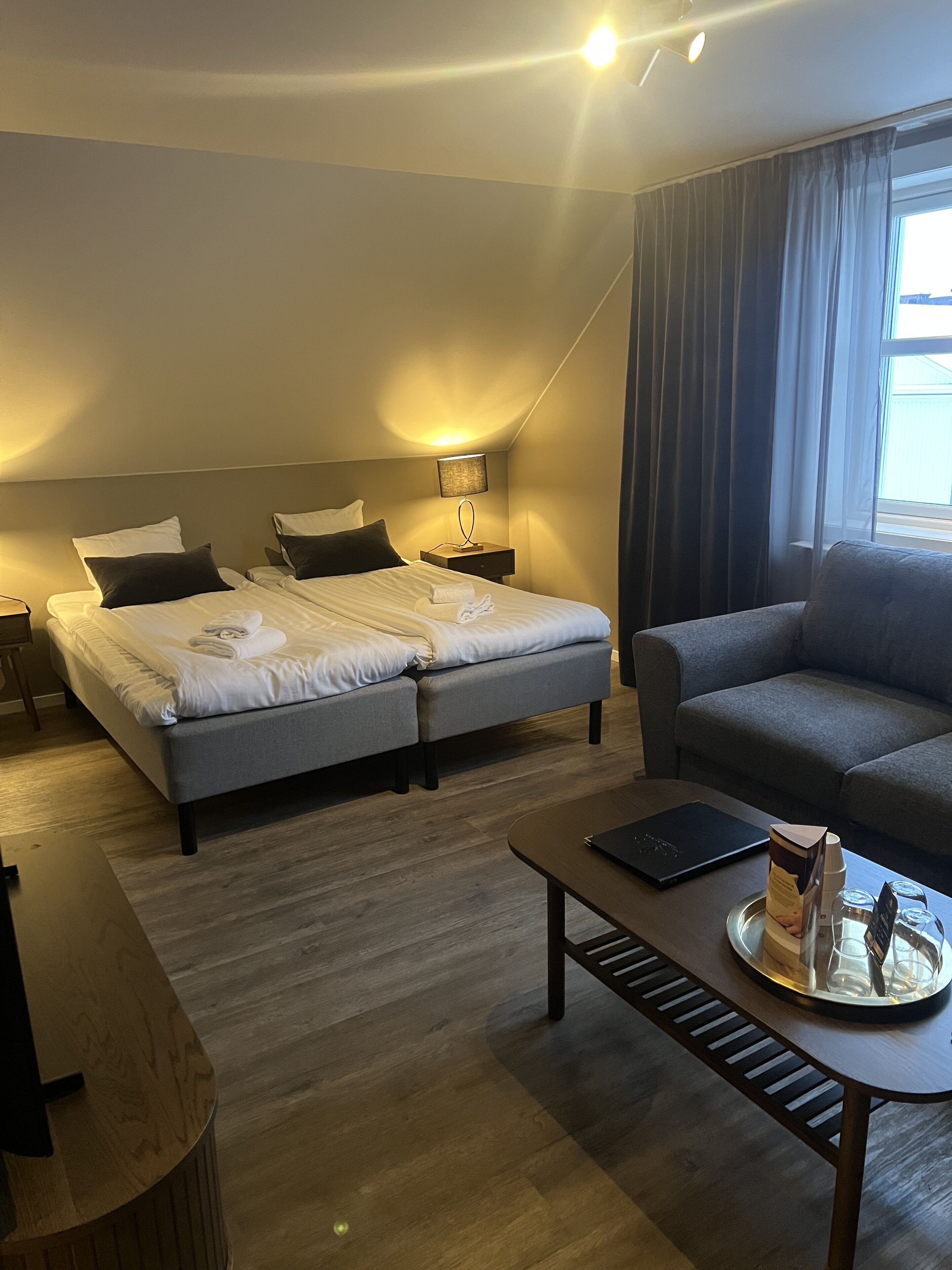 A hotel room with a double bed, a sofa, a coffee table with a tray, and a lamp.