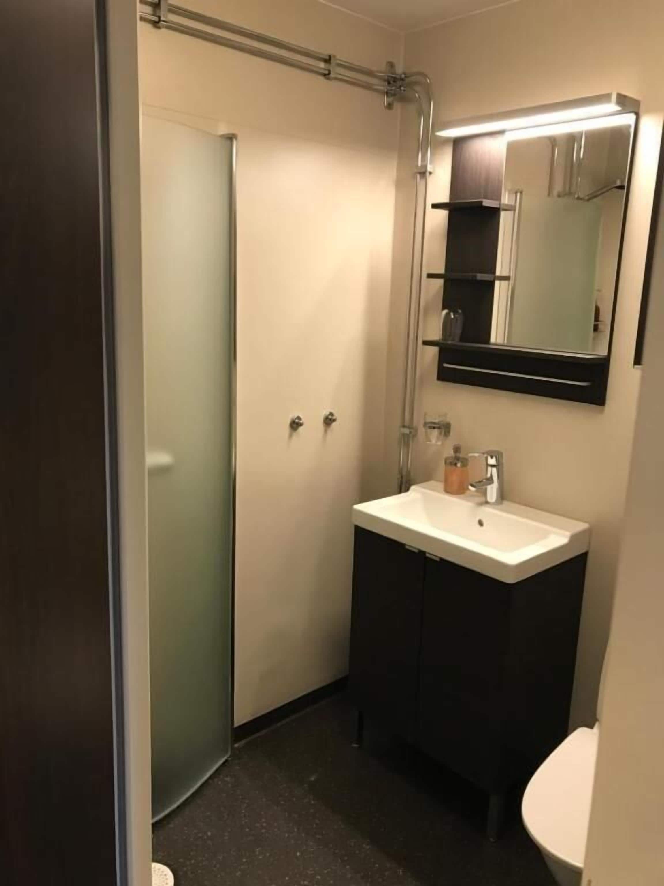 A bathroom with a white sink, dark cabinets, a mirror, and a shower door.