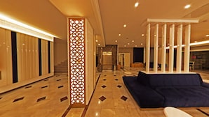 A spacious lobby with a high ceiling, a central column with intricate cut-out patterns, a blue sofa, and a patterned floor. - Mara Palas Hotel (Fethiye)
