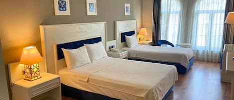 A hotel room with two beds, a nightstand with a lamp, a desk, and a chair.