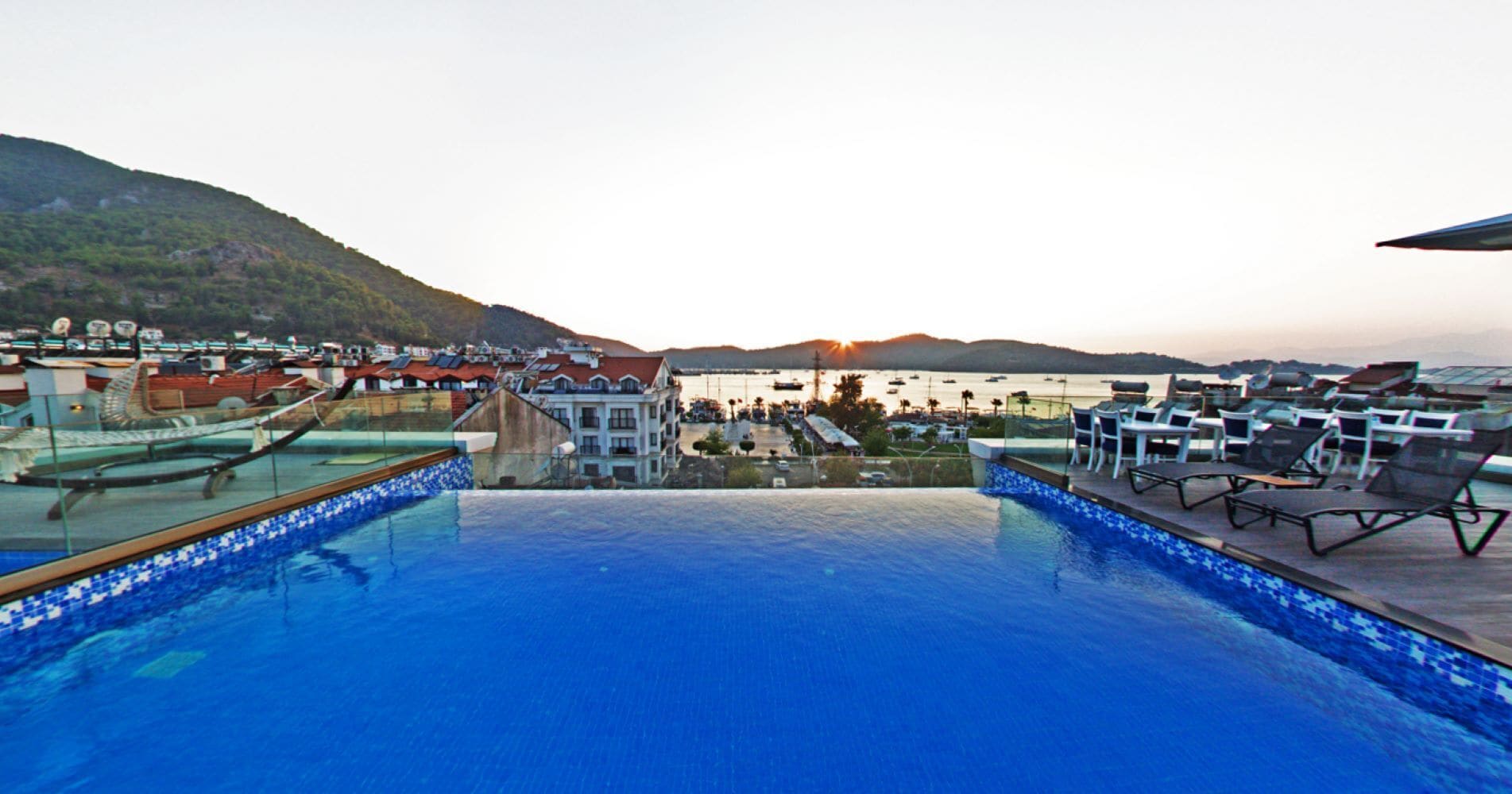A rooftop infinity pool with a view of a marina and hills.