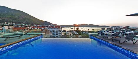 A rooftop infinity pool with a view of a marina and hills.