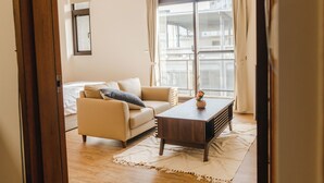 Una habitación con sofá, una mesita, una ventana con cortinas y vistas a edificios.
