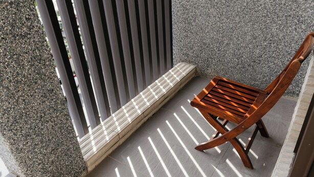 Una silla de madera sobre un piso de baldosas, con un banco de listones y una valla metálica vertical.