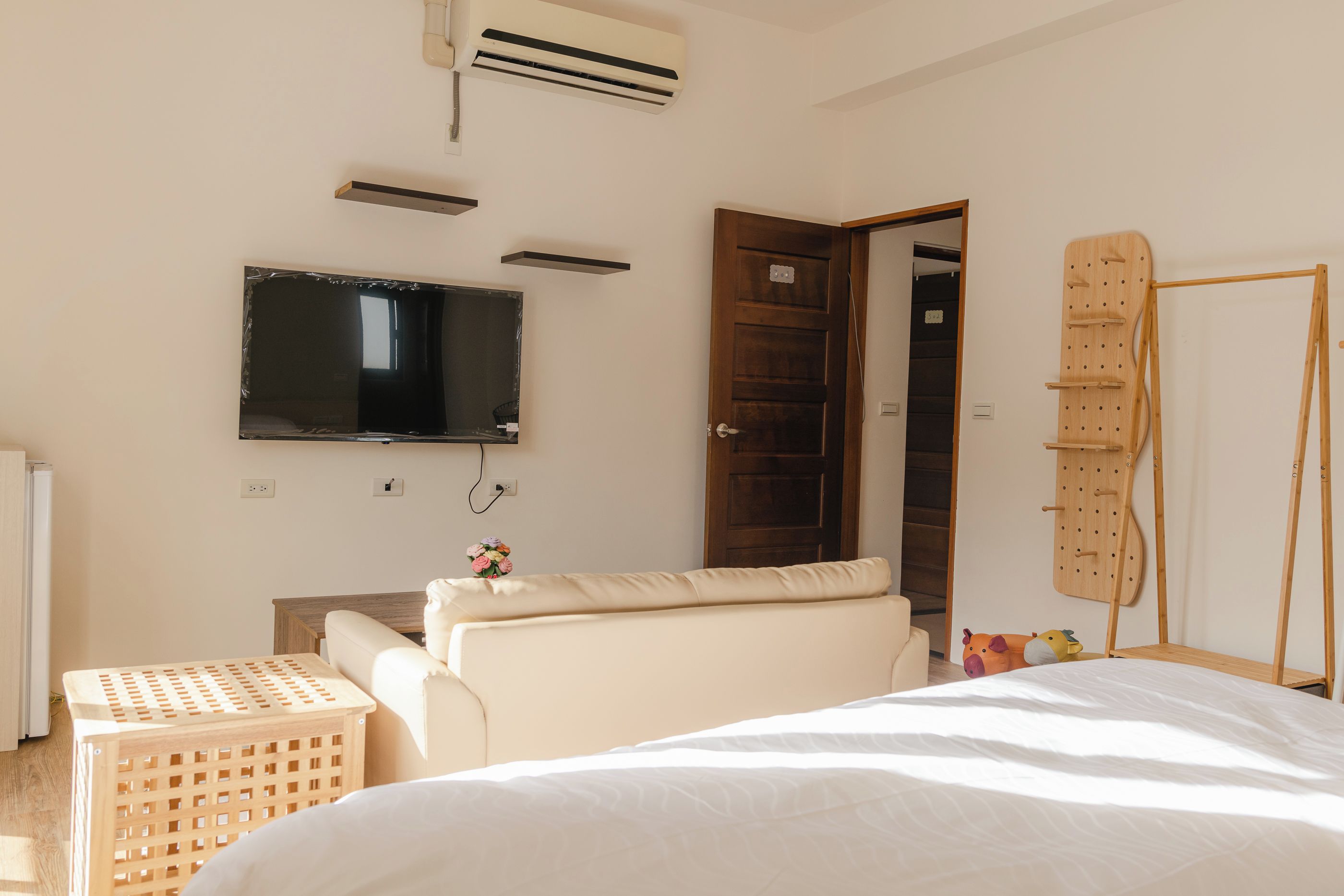 A bedroom with a bed, a television, a wooden door, and a wall-mounted drying rack.