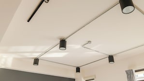 Techo con varias luces de riel y un ventanal con cortinas.