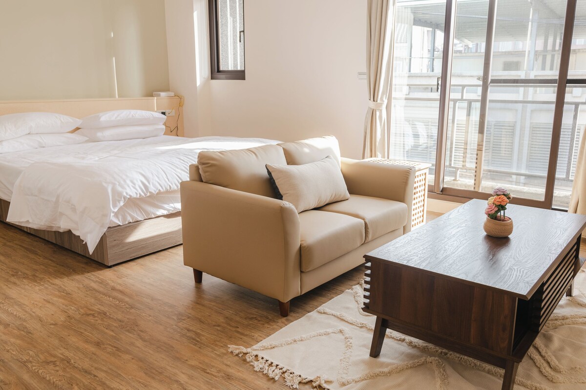 Une chambre d’hôtel avec un lit, un canapé, une table basse en bois et une vue par la fenêtre.