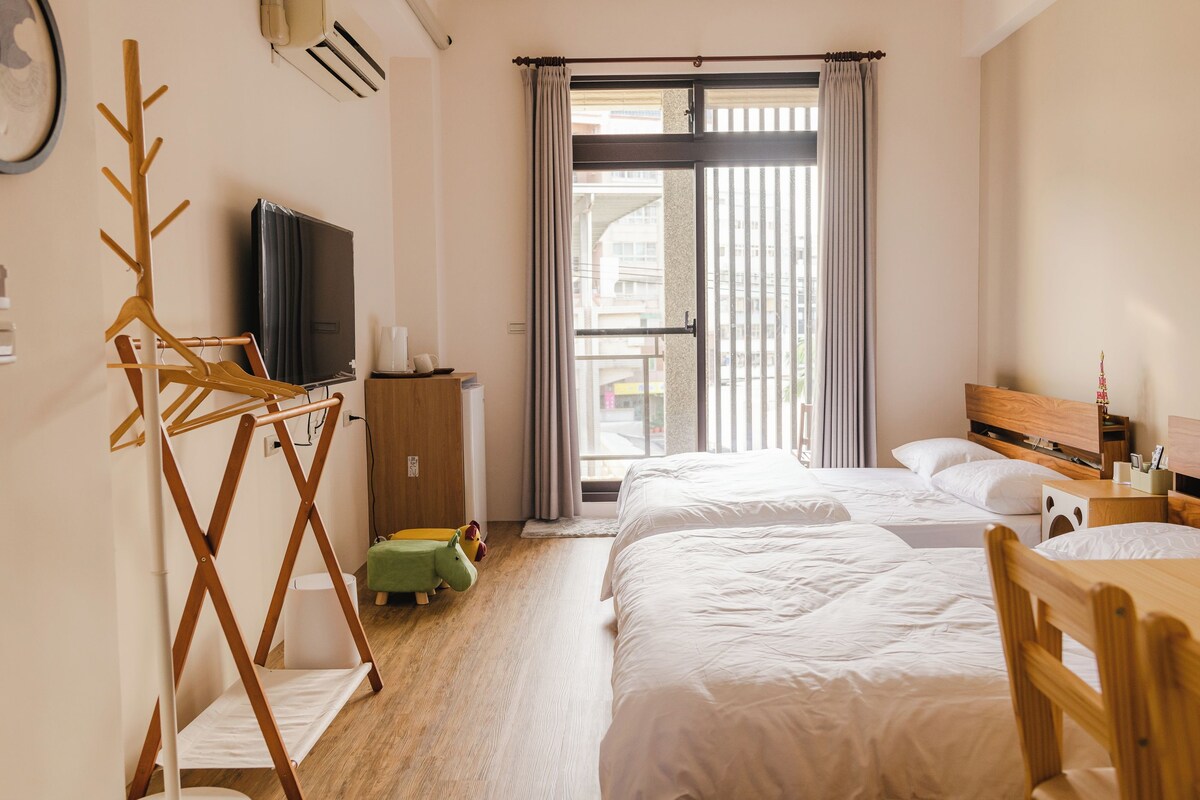 Une chambre d’hôtel avec deux lits, une télévision, un porte-manteau en bois, une petite table et une fenêtre avec des rideaux.