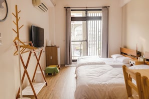 Une chambre d’hôtel avec deux lits, une télévision, un porte-manteau en bois, une petite table et une fenêtre avec des rideaux.