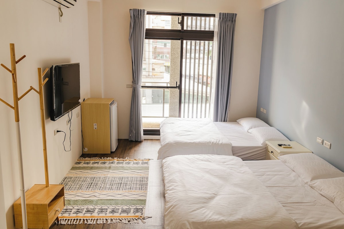 Une chambre d’hôtel avec deux lits, une télévision, un porte-manteau en bois et une fenêtre avec des rideaux.