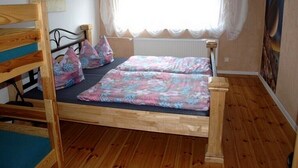 A wooden bunk bed with a floral bedspread, a window with sheer curtains, and a painting on the wall.