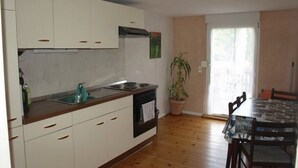 A kitchen with white cabinets, a sink, and an oven. There is a dining table with chairs and a potted plant.