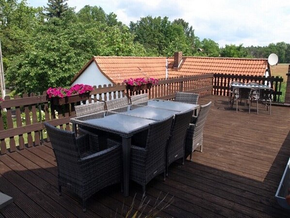 A deck with wicker furniture and a table, surrounded by a wooden fence and a house with a tiled roof.
