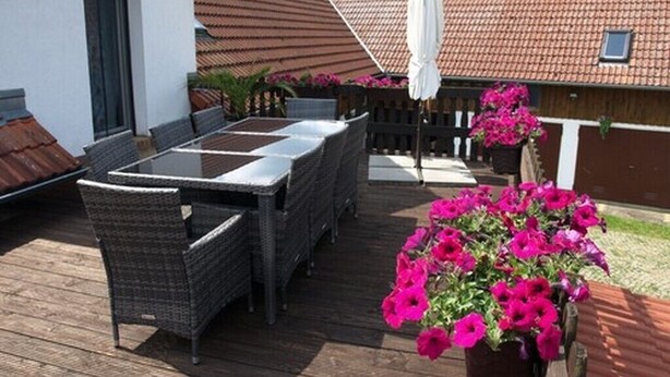 An outdoor patio with a table and chairs, surrounded by potted plants and a wooden fence.