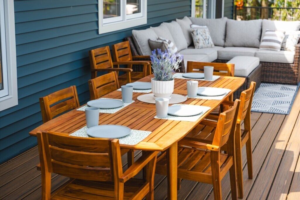 A wooden deck with a dining table set for four, surrounded by wooden chairs.
