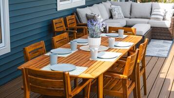 A wooden deck with a dining table set for four, surrounded by wooden chairs.