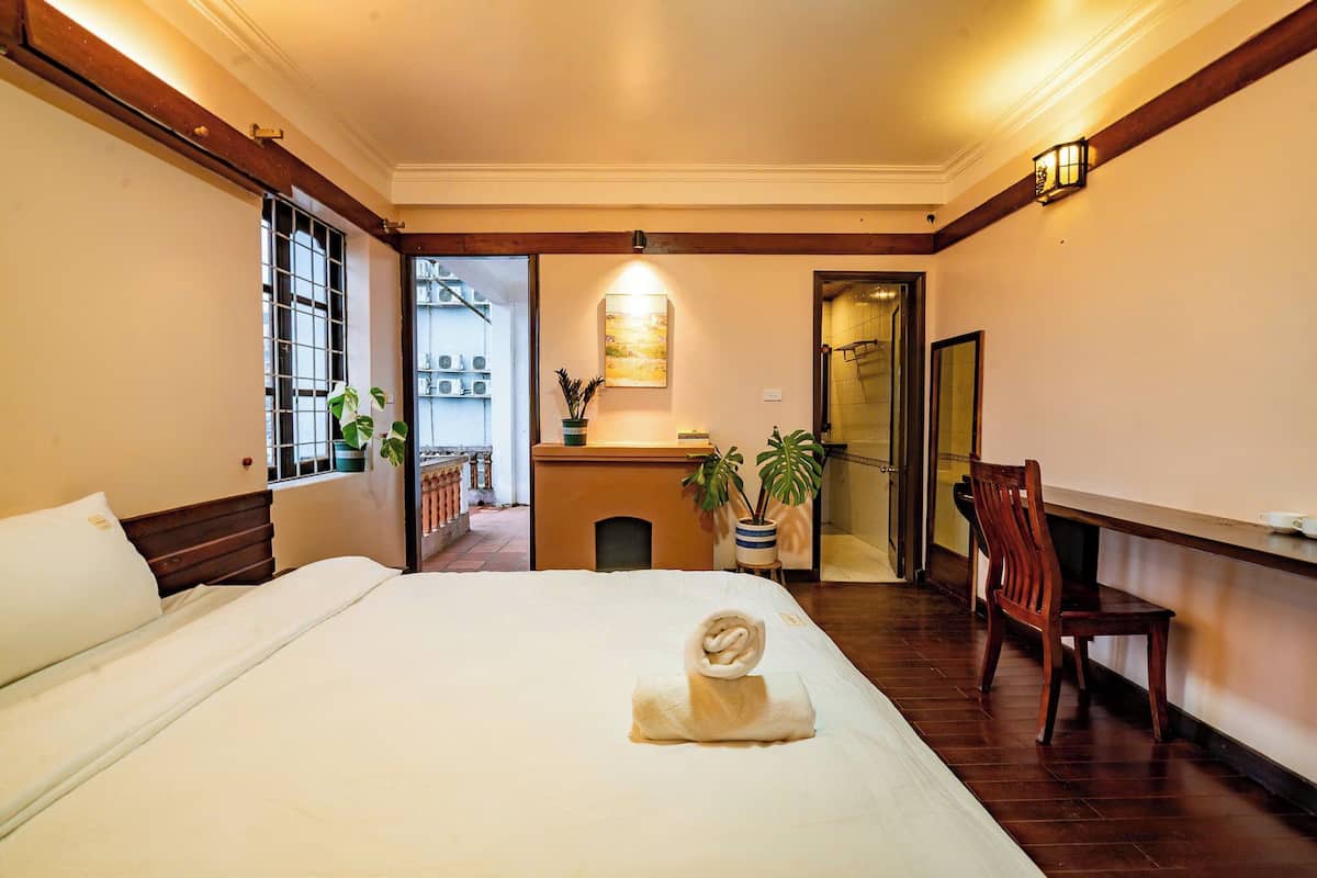 A hotel room with a bed, a desk, a chair, and a potted plant.