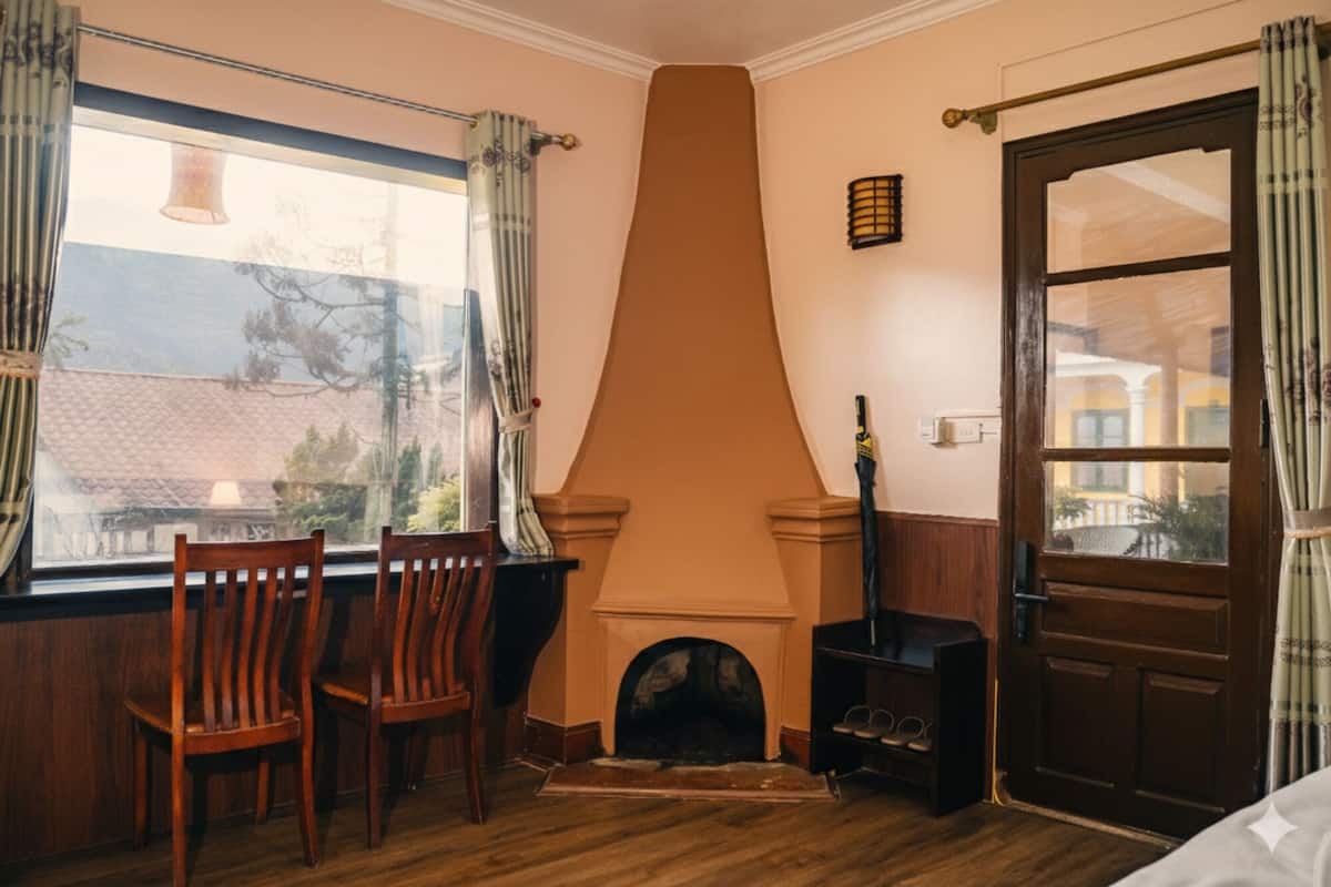 A room with a fireplace, wooden chairs, a window with curtains, and a door.