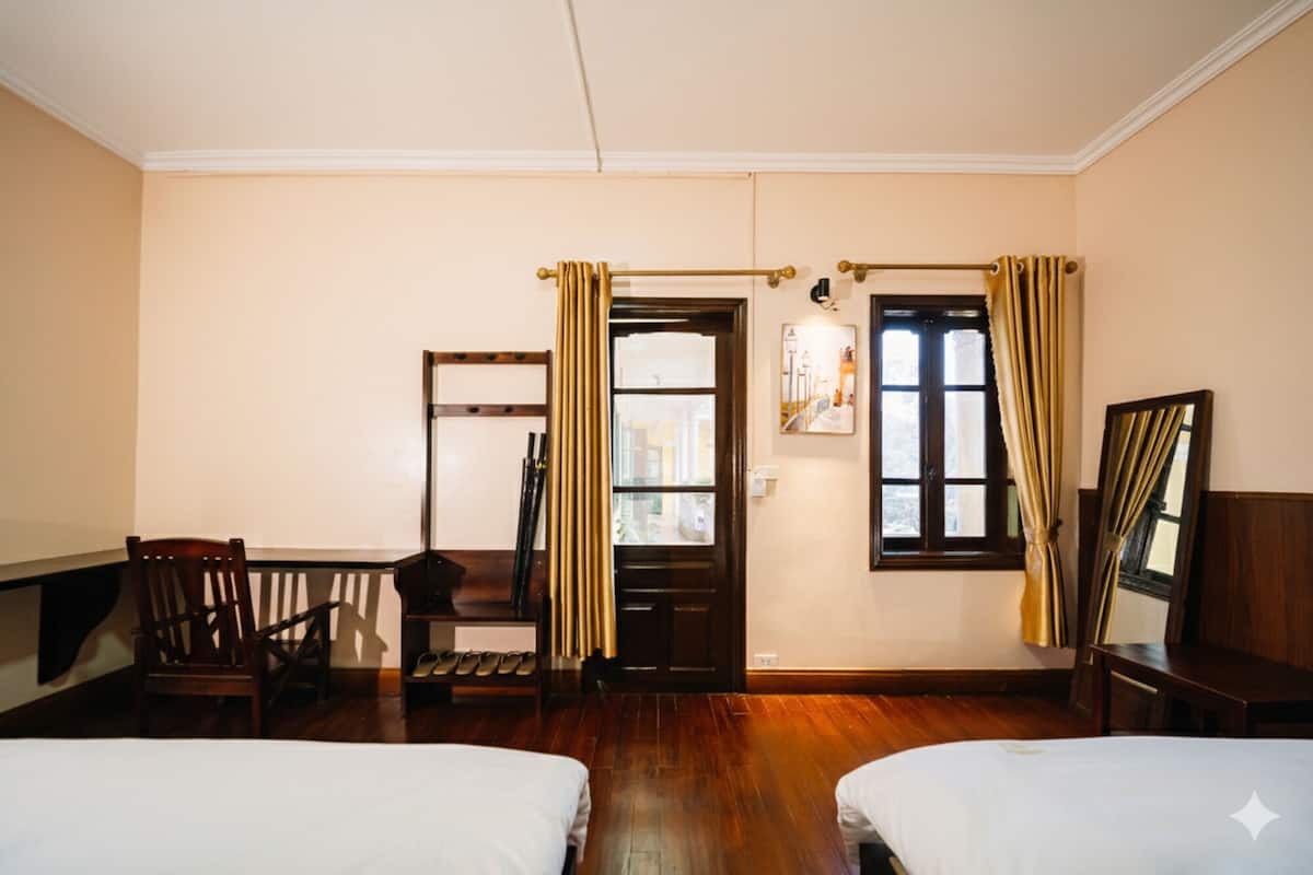 A hotel room with two beds, a wooden chair, a coat rack, and a window with curtains.