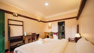 A hotel room with a bed, a desk, a chair, a lamp, and a green door.