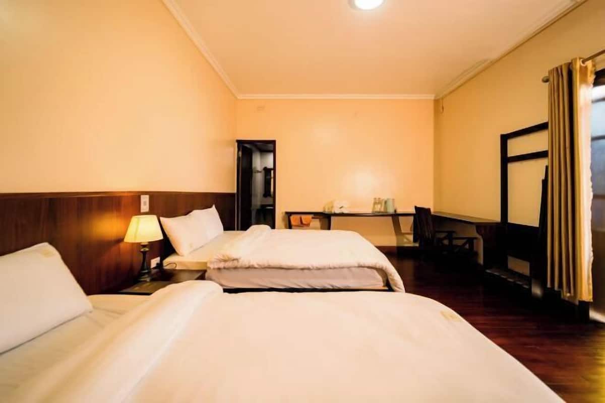 A hotel room with two beds, a desk, a chair, a lamp, and a mirror.