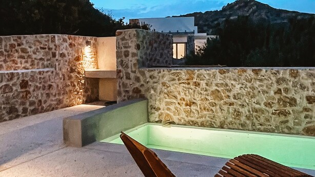 A stone-walled outdoor area with a pool and a wooden lounge chair. - Themis Homes Thallo  in Skyros (Skyros)
