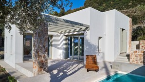 A modern house with a swimming pool, stone pillars, and a wooden bench. - Themis Homes Thallo  in Skyros (Skyros)