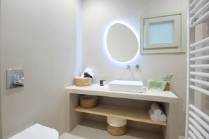 Een badkamer met een witte wastafel, een spiegel met verlichting, een handdoekhouder en rieten manden.
