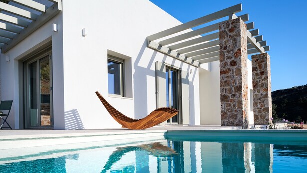 Un espace moderne aménagé au bord de la piscine, avec une piscine à eau claire, un hamac en bois et un pilier en pierre.