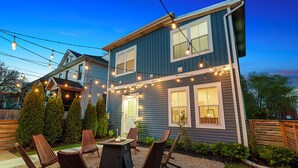 Een tweelaags huis met een patio, inclusief tuinmeubilair en lichtslingers.