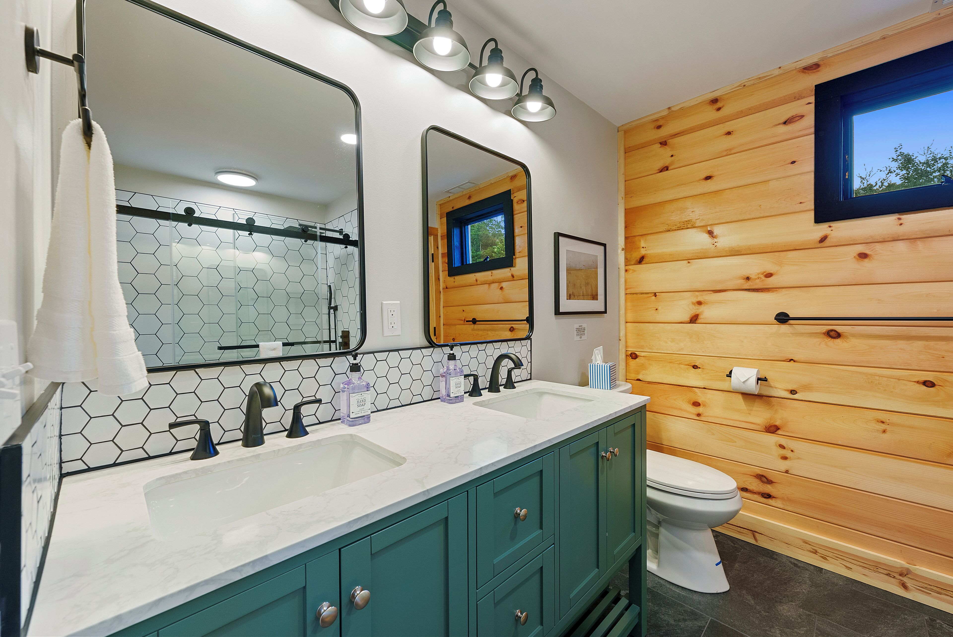A bathroom with a wooden wall, a large mirror, a sink with two faucets, and a toilet.
