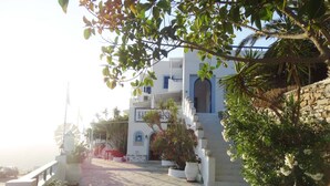 A white building with blue accents, a stone-paved pathway, and potted plants. - Castelopetra Studios (Amorgos)