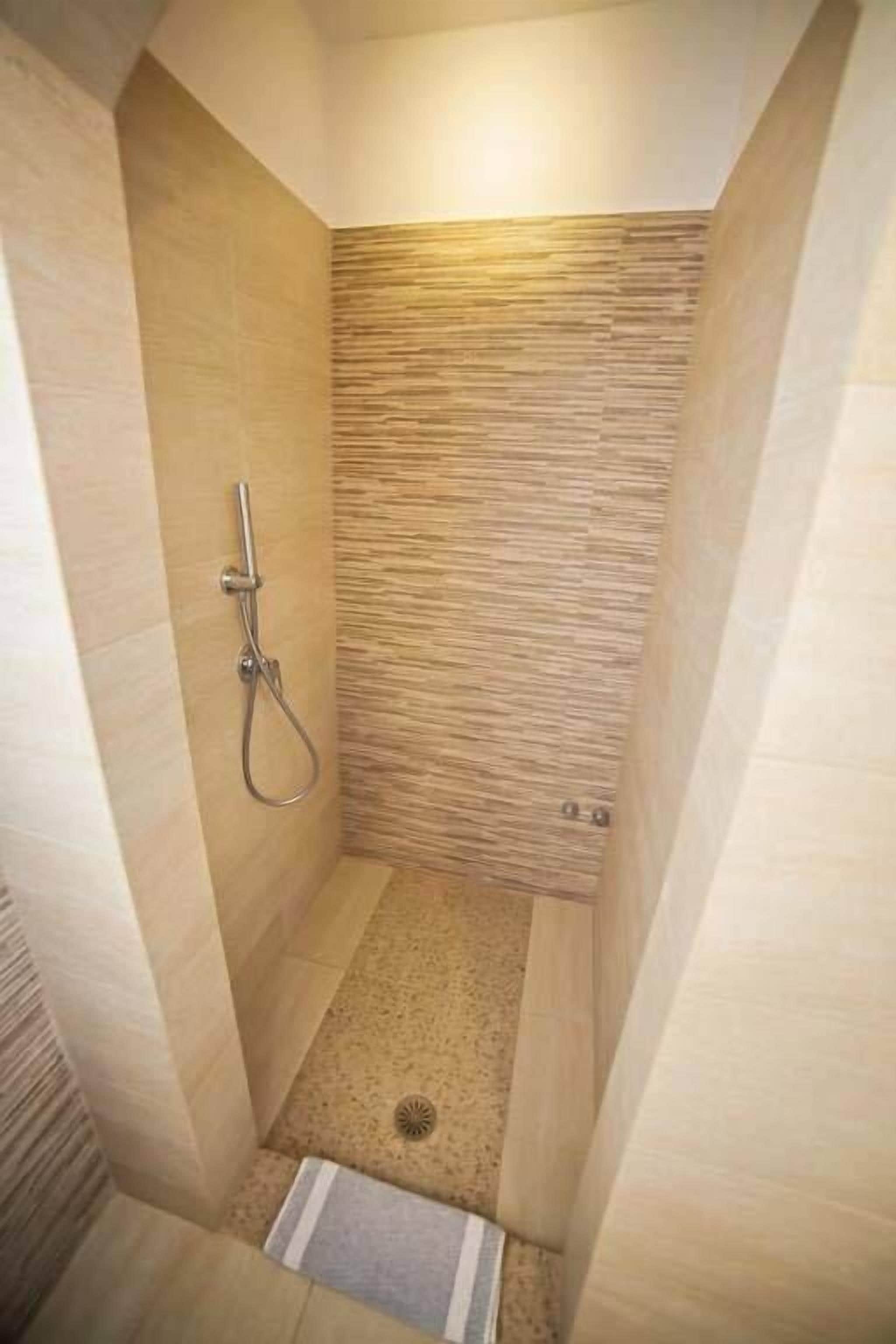 Une petite salle de douche étroite, avec un mur à texture et un pommeau de douche.