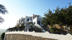 A white building with multiple balconies and a stone wall. - Castelopetra Studios (Amorgos)